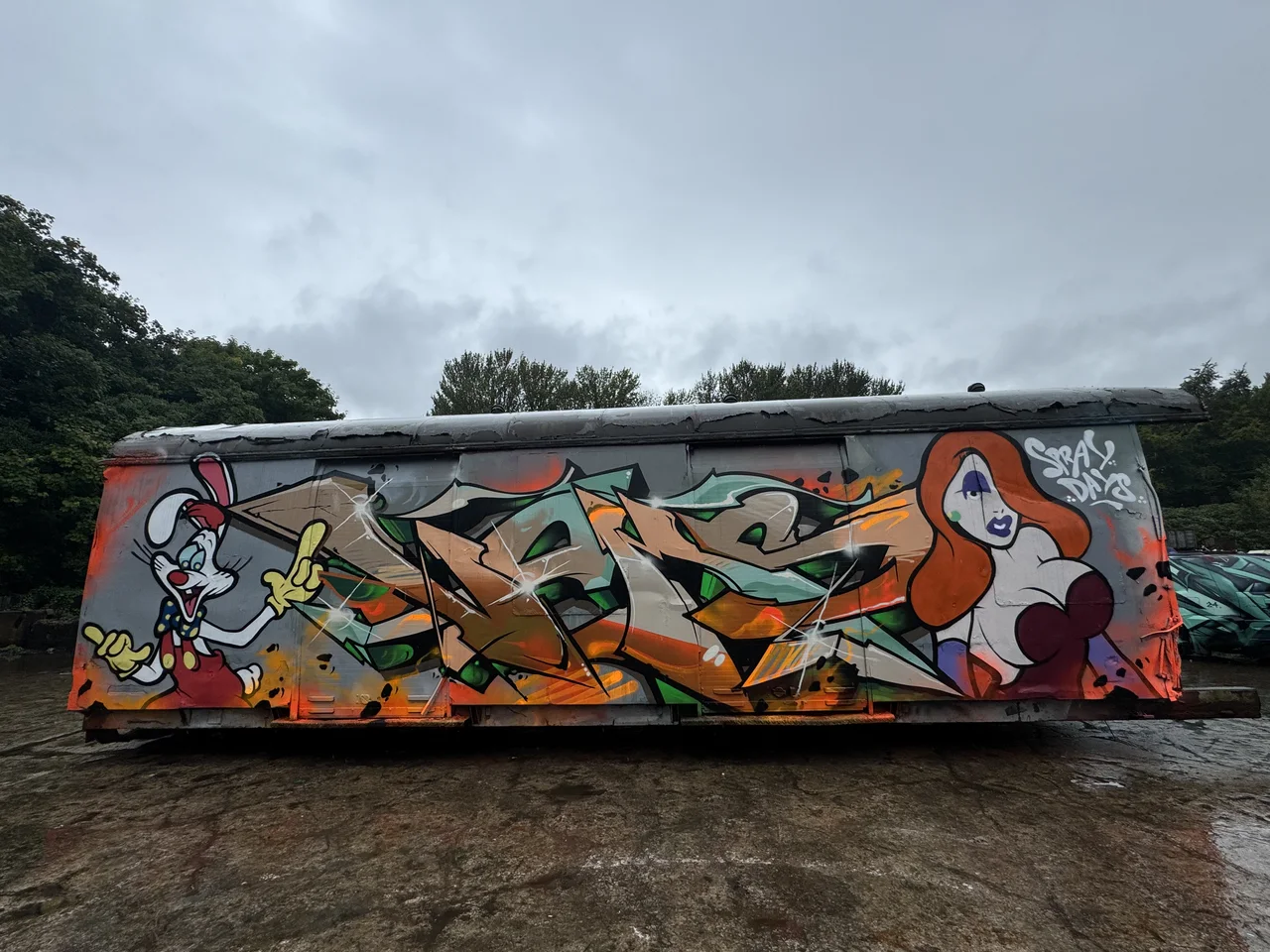 A scrapyard trailer covered in orange, green and white graffiti.