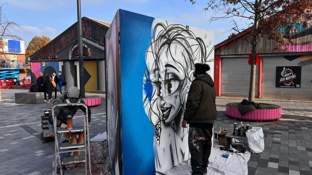 A painter working on a black-and-white portrait on a blue panel in Lyceum Square.