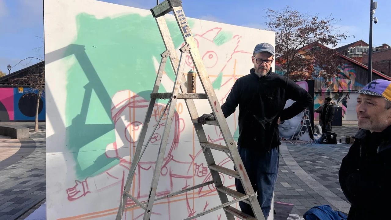 People beside a stepladder and a panel with mint-green paint and red figure outlines in Lyceum Square.