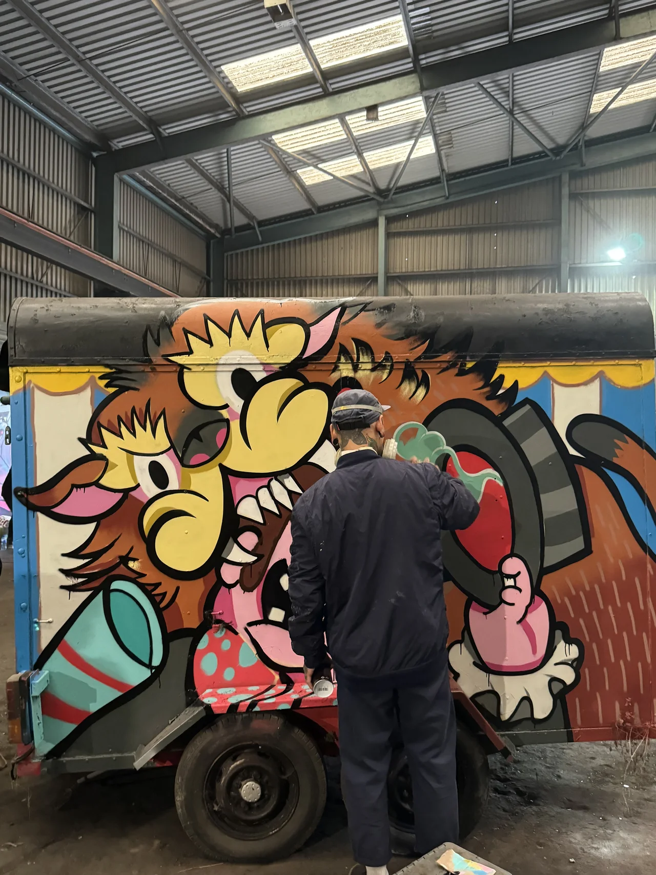 An artist painting a bright cartoon composition on a large workshop panel.