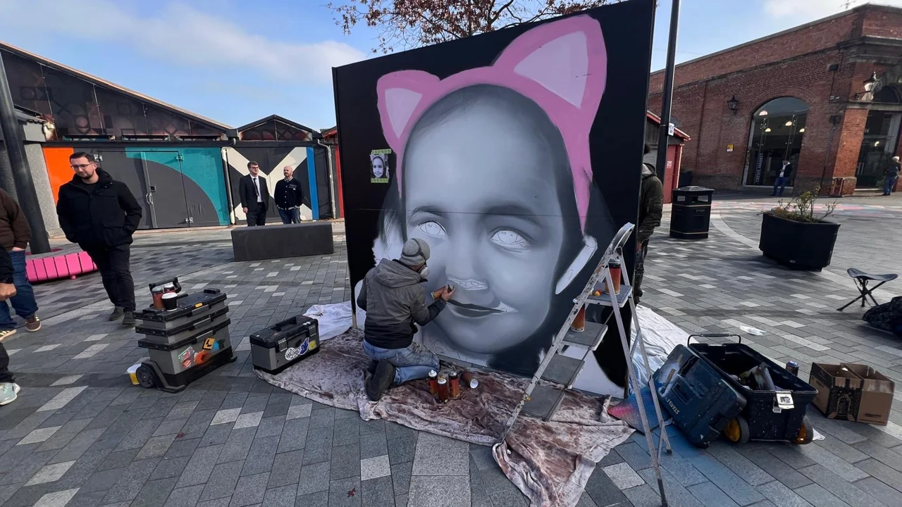 A portrait with pink cat ears on a freestanding panel in Lyceum Square, with paint cans arranged below.