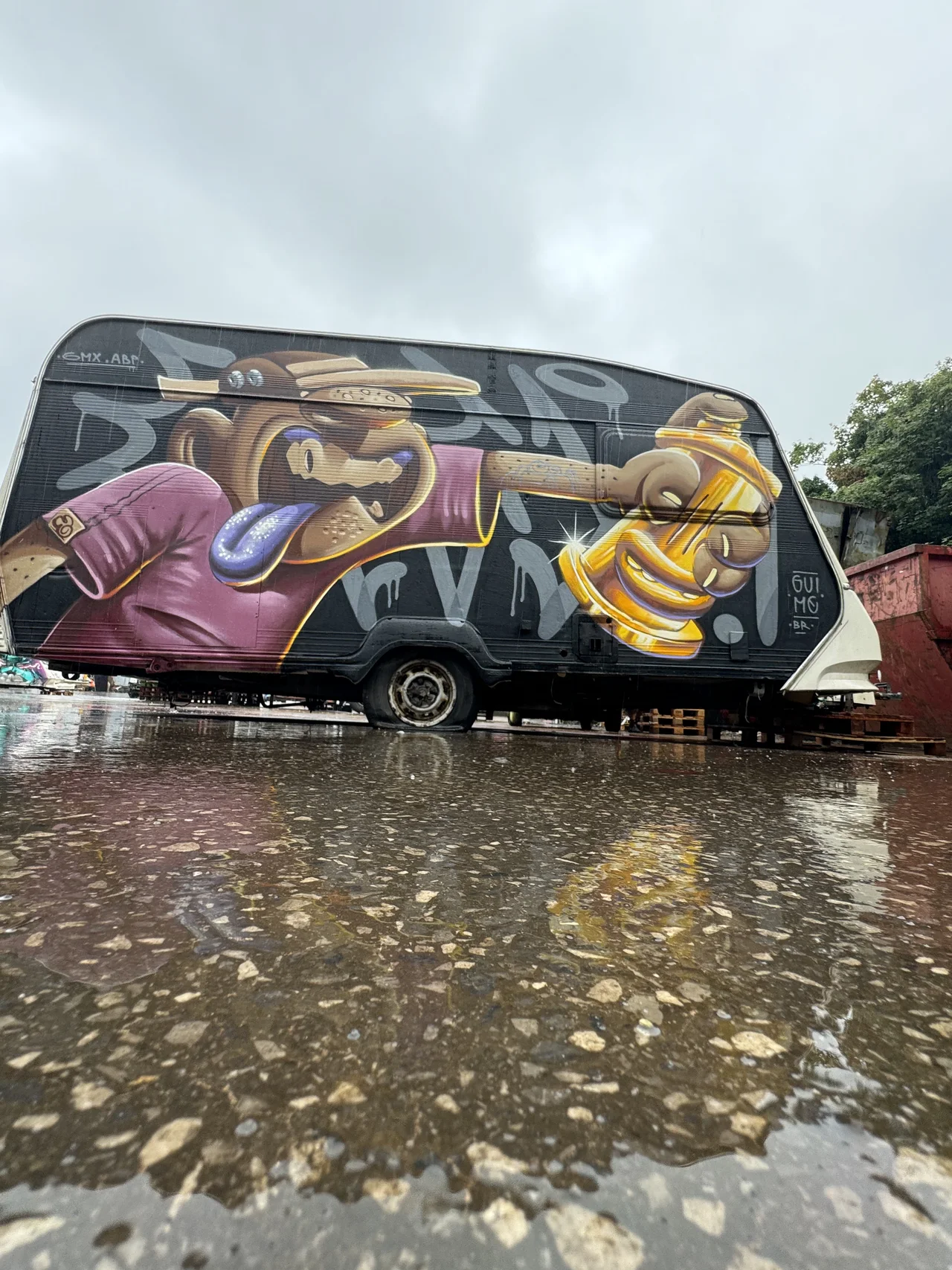 Colourful graffiti covers a van in the scrapyard beside a puddle.