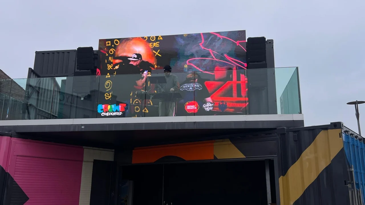 A large outdoor screen displaying CreweColours imagery above a colourful building in Lyceum Square.