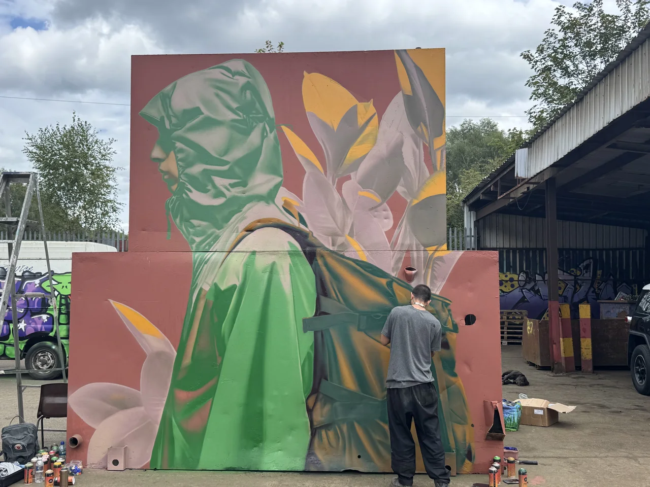 An artist beside a tall green and orange geometric portrait panel outdoors.