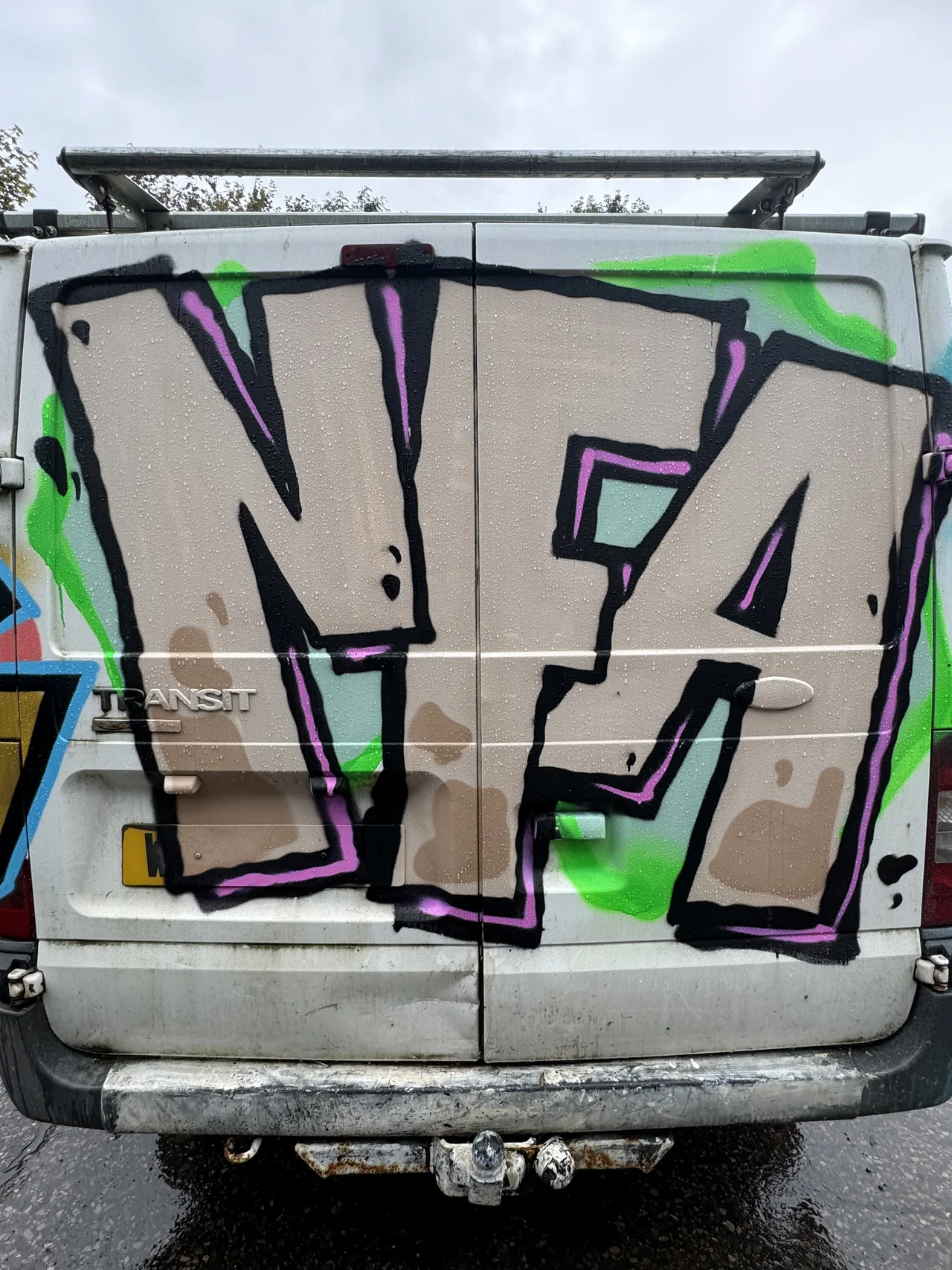 The rear of a white van painted with large outlined graffiti letters.