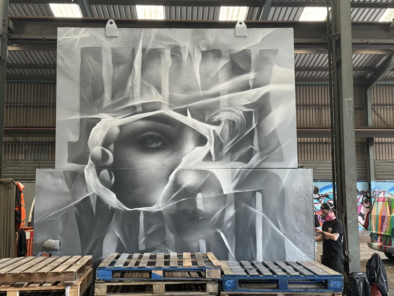 A large monochrome portrait panel inside the scrapyard workshop.