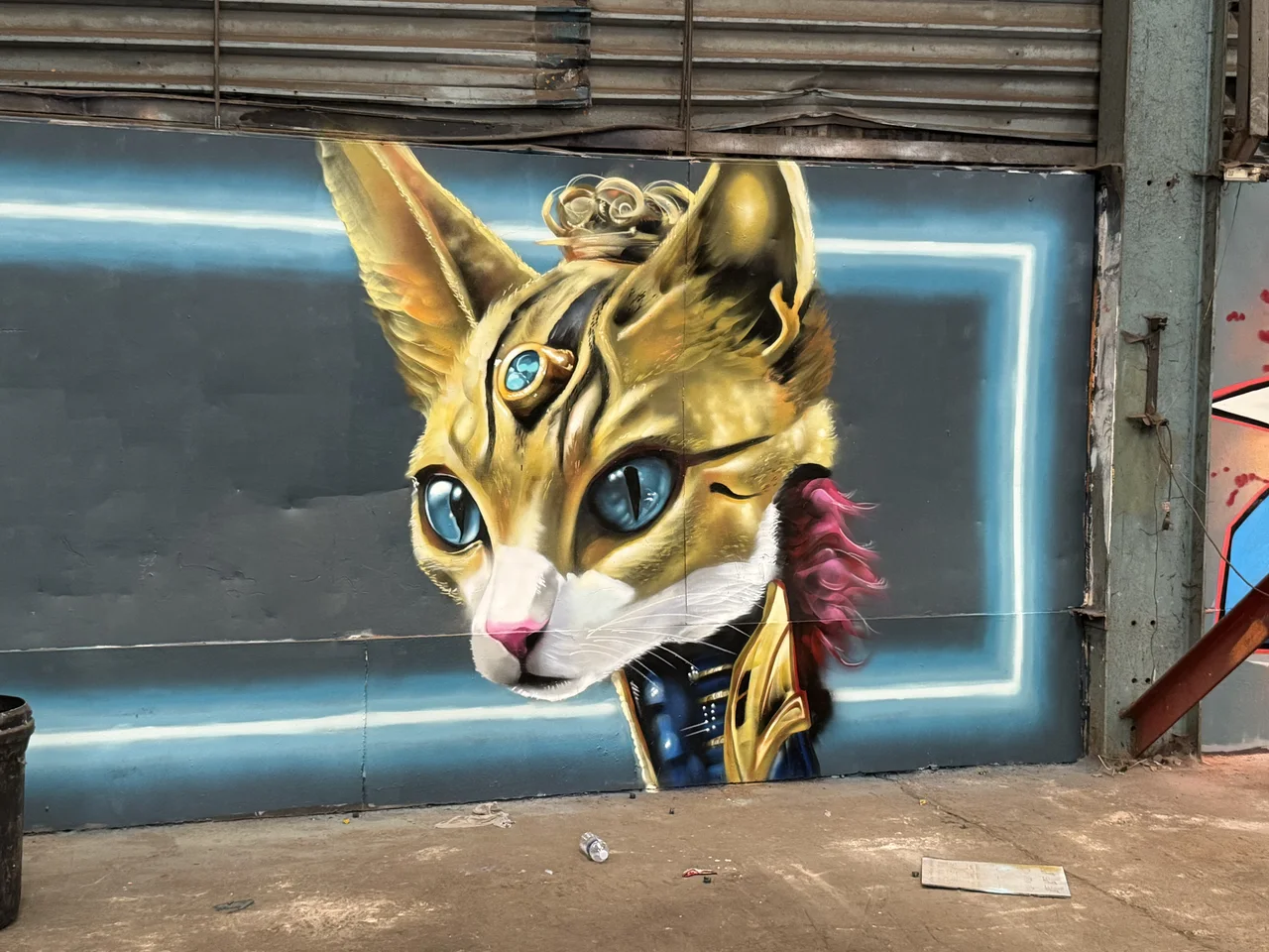 A painted cat wearing an ornate gold headdress against a dark blue panel.