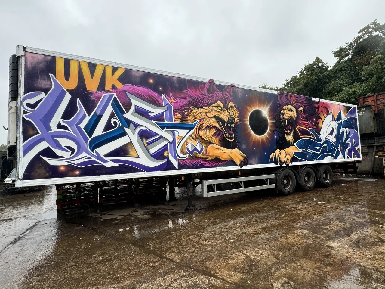 A long lorry trailer covered in purple lettering and a painted figure.